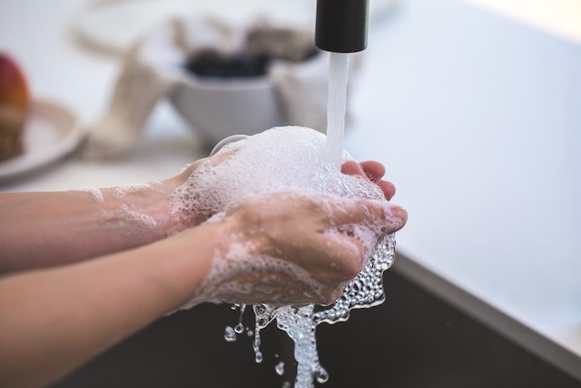 Człowiek myjący ręcę pod odkręconym kranem
